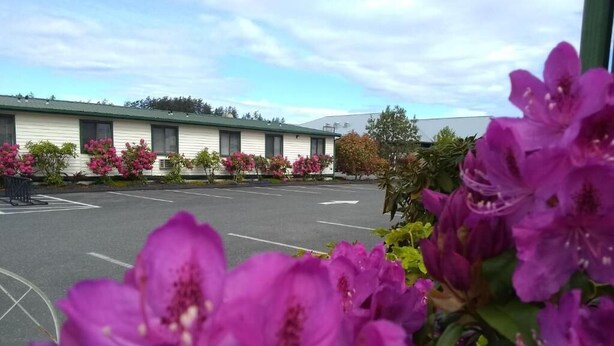 A motel with a row of rooms, a parking lot, and blooming flowers in the foreground. - The Orca Inn (Friday Harbor)