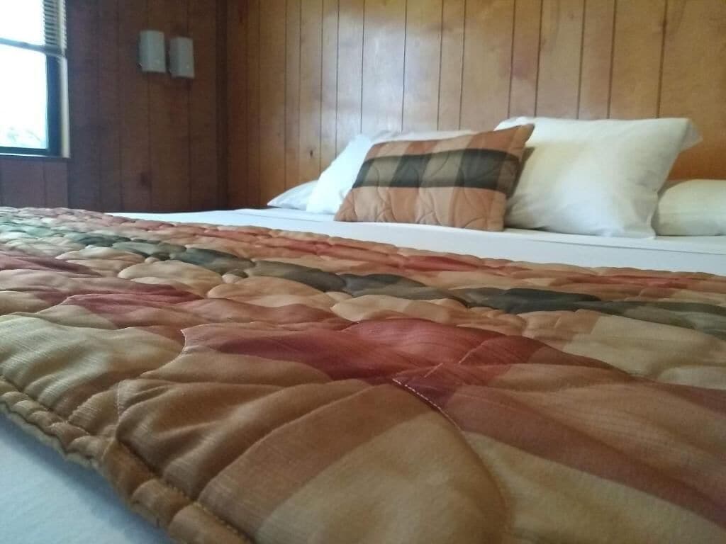 Un lit avec une couette aux couleurs vives, une tête de lit en bois et une fenêtre avec des stores.