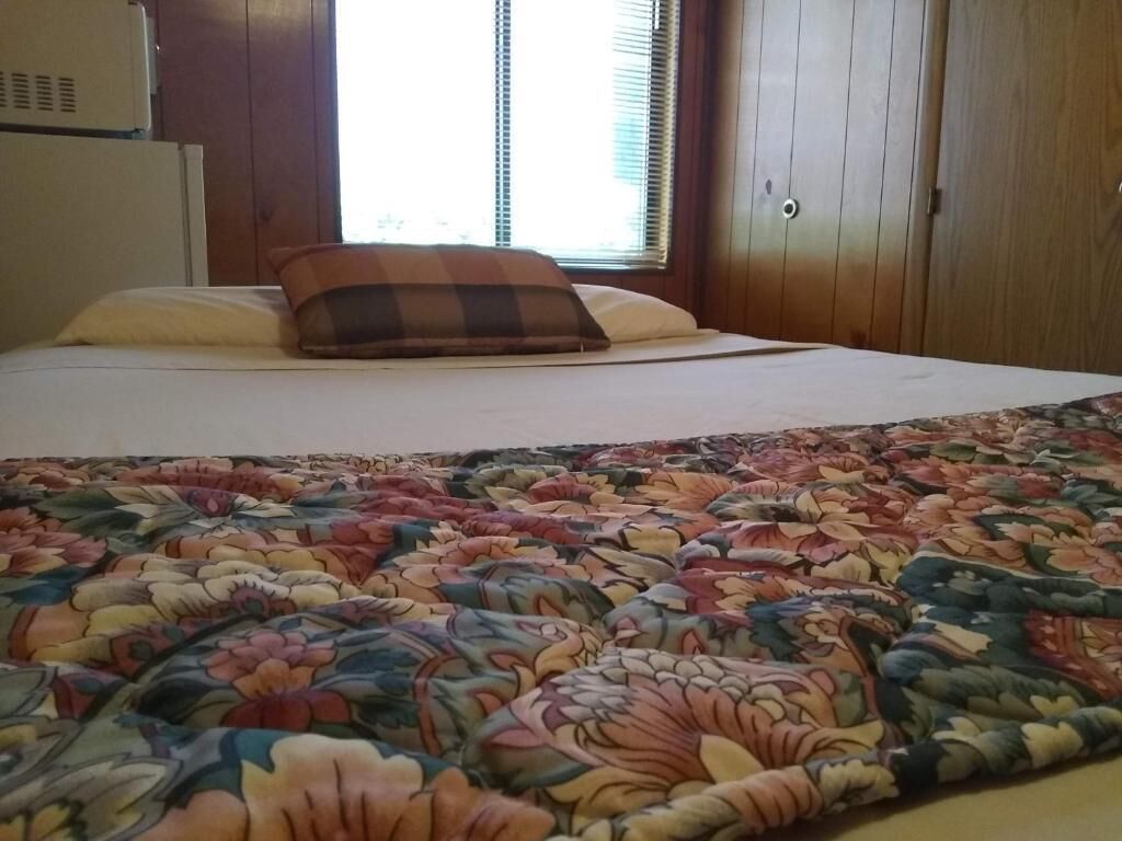 A bed with a floral-patterned bedspread, a plaid pillow, and a window with blinds.