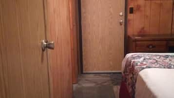 Een hotelkamer met een houten deur, een bed met een bedovertrek met patroon, een klein houten dressoir en een flatscreen televisie aan de muur.