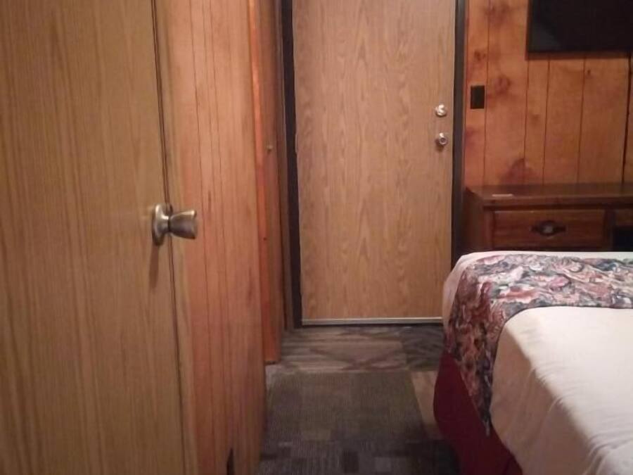 Een hotelkamer met een houten deur, een bed met een bedovertrek met patroon, een klein houten dressoir en een flatscreen televisie aan de muur.