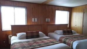 A room with two beds, wooden panel walls, and two windows with blinds.