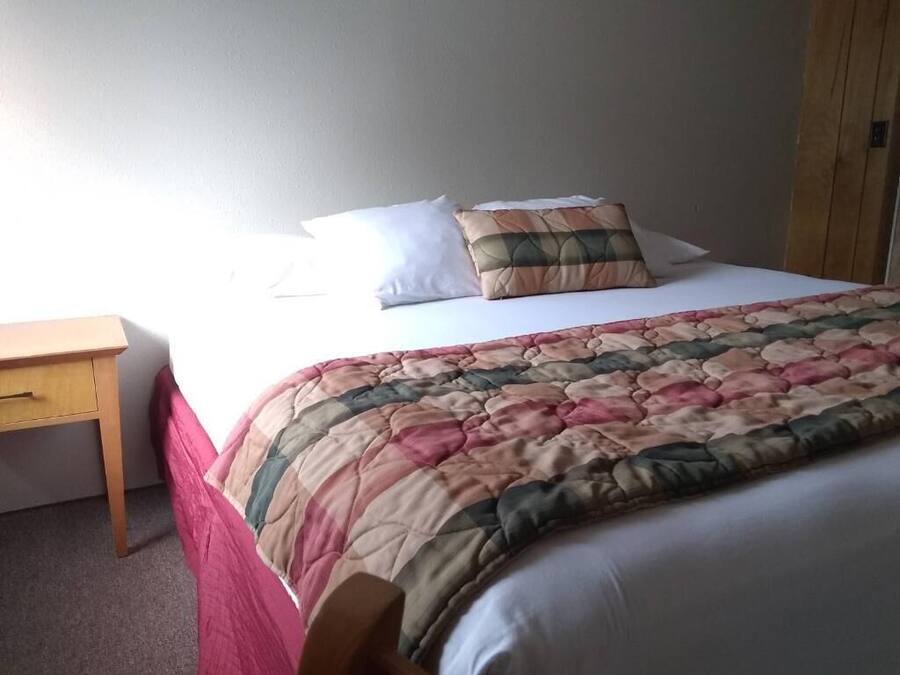 Een bed met een sprei, een houten nachtkastje en een kledingkast.