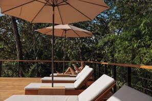 A deck with lounge chairs and an umbrella, surrounded by dense foliage. - Sunrise Studio at Taru Rentals Ocean Views (Montezuma)