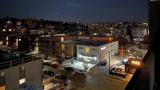 Vue nocturne d’un quartier résidentiel avec des immeubles, un parking et une enseigne bien visible d’une pizzeria.