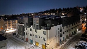 Un immeuble à plusieurs étages, doté d’un toit plat, de plusieurs balcons et d’un parking où sont garées des voitures.