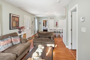 Un salon avec un canapé marron, une table basse et un coin repas comprenant une table et des chaises blanches.