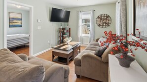 A living room with a sofa, a coffee table, a TV, and a window with curtains. - Cozy 2-bedroom house in perfect Westerly with AC. Big,  open back yard! (Westerly)