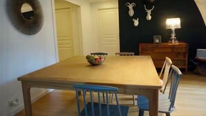 Un comedor con mesa de madera, sillas azules, frutero y lámpara sobre un aparador.