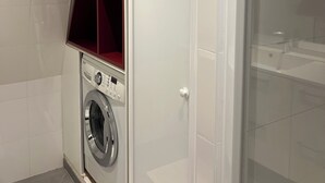 Un lavadero pequeño con lavadora, estante empotrado y cabina de ducha de vidrio.