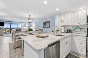 A modern kitchen with white cabinetry, a marble countertop, and a built-in dishwasher. - Sunrise to Sunset | Oceanfront Amelia Condo with insane views! (Fernandina Beach)
