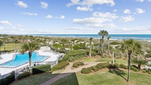 Zona de piscina con vista al océano, rodeada de palmeras y un cielo despejado.