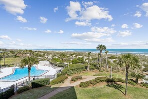 A pool area with a view of the ocean, surrounded by palm trees and a clear sky. - Sunrise to Sunset | Oceanfront Amelia Condo with insane views! (Fernandina Beach)