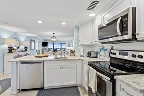 A modern kitchen with white cabinetry, a built-in oven, a microwave, and a large island with a sink. - Sunrise to Sunset | Oceanfront Amelia Condo with insane views! (Fernandina Beach)