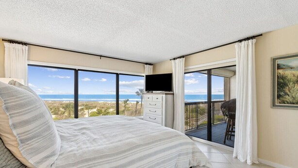 Un dormitorio con cama, televisor, cómoda y balcón con vista al océano.