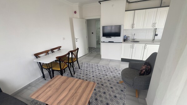 A compact living space with a dining area, a sofa, a TV, and a kitchenette.