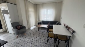 A modern living space with a sofa, dining table, chairs, and a refrigerator.