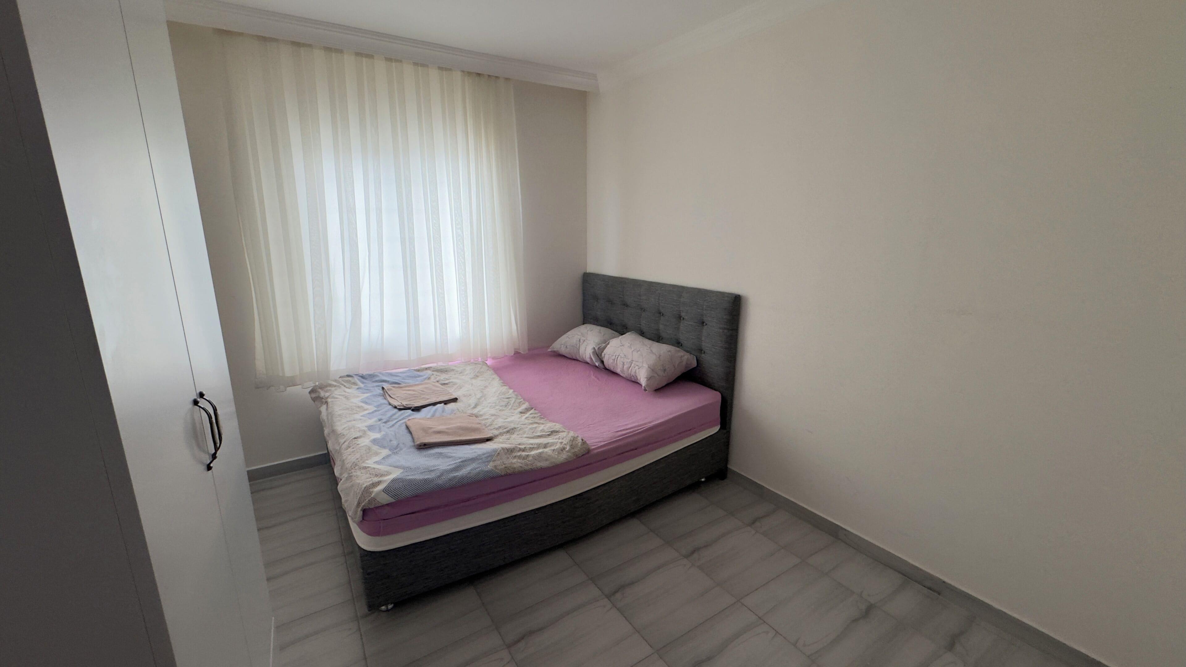 Un dormitorio con cama, ventana con cortinas y puerta.