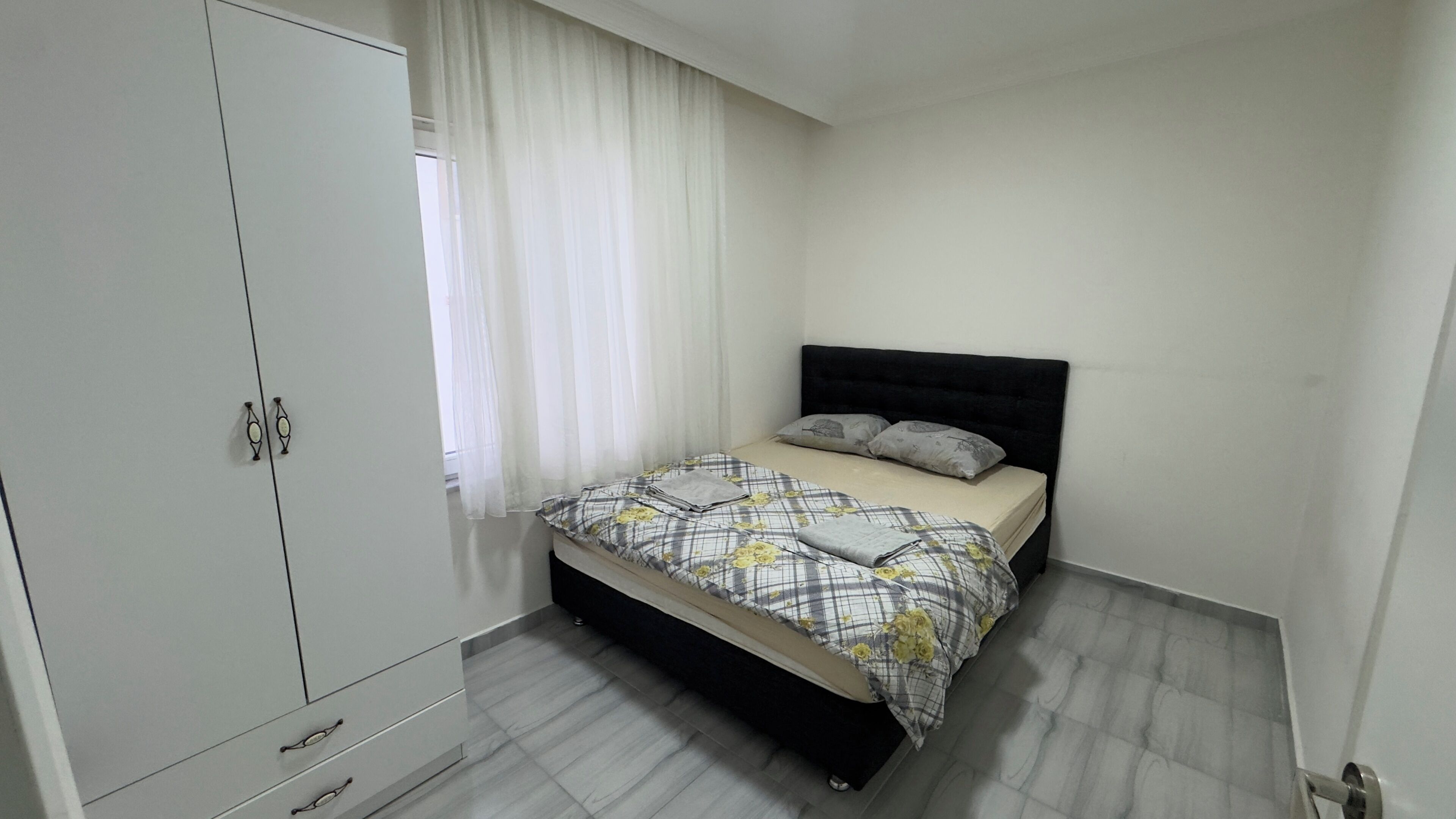 A bedroom with a bed, a wardrobe, and a window with curtains.