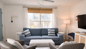 A living room with a blue sofa, two armchairs, a coffee table, a TV, and a balcony view. - Show Me Carolina, Steps to Beach, Pet Friendl (Topsail Beach)