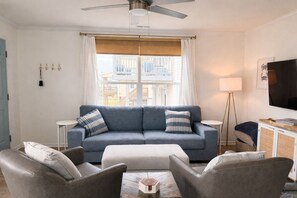 A living room with a blue sofa, two armchairs, a coffee table, a TV, and a balcony view.