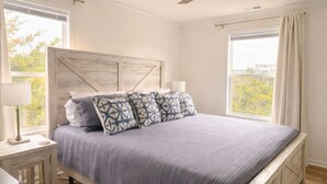 A bedroom with a bed, a nightstand, a lamp, a ceiling fan, and large windows. - Show Me Carolina, Steps to Beach, Pet Friendl (Topsail Beach)