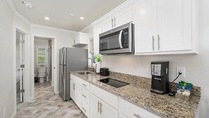 A modern kitchen with white cabinets, a stainless steel refrigerator, a built-in microwave, a coffee maker, and a granite countertop. - Jellystone Park Delaware Beaches (Lincoln)