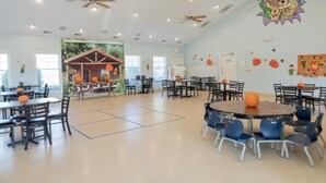 A spacious indoor area with multiple tables and chairs, ceiling fans, and a mural on the wall. - Jellystone Park Delaware Beaches (Lincoln)