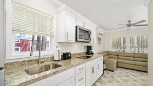 A modern kitchen with white cabinets, a granite countertop, a stainless steel sink, a microwave, and a ceiling fan. - Jellystone Park Delaware Beaches (Lincoln)