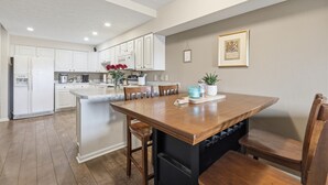 A kitchen with white cabinets, a wooden dining table, and a potted plant.