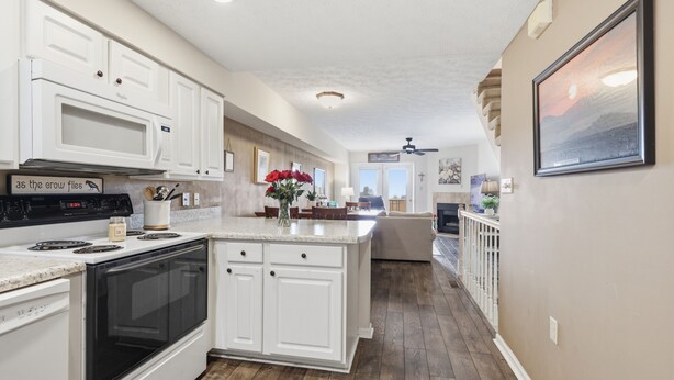 A kitchen with white cabinets, a stove, and a microwave. There is a dining area with a table and chairs.