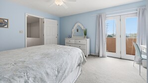 A bedroom with a bed, a ceiling fan, a dresser, a mirror, a door, and a balcony with curtains.