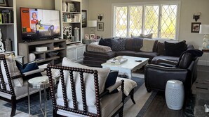 Una sala de estar con un sofá, sillas, una mesa de centro, un televisor y una estantería.