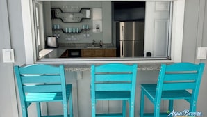 A kitchen with a built-in refrigerator, a coffee maker, and a set of blue chairs.