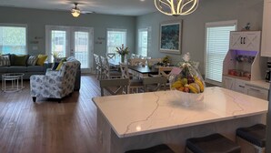 A modern kitchen with a marble island, dining area, and a ceiling fan.