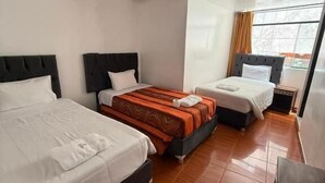 Een hotelkamer met drie bedden, een houten vloer en een raam met gordijnen.