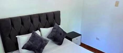 Una cama con cabecera capitonada, ropa de cama blanca y dos almohadas. Una toalla está colocada sobre la cama.