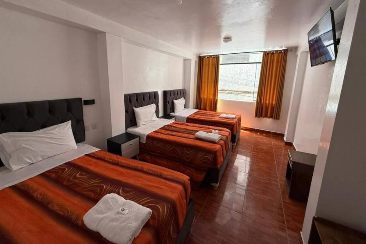 Habitación de hotel con una cama grande, una cama más pequeña, una mesita de noche, un televisor y una ventana con cortinas.