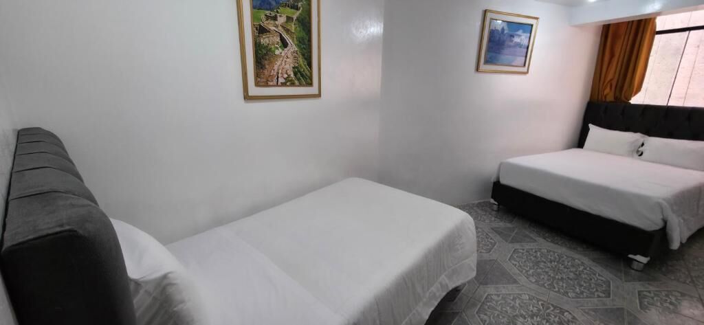 Een hotelkamer met twee enkele bedden, een bank, een kleine tafel en twee ingelijste foto’s aan de muur.