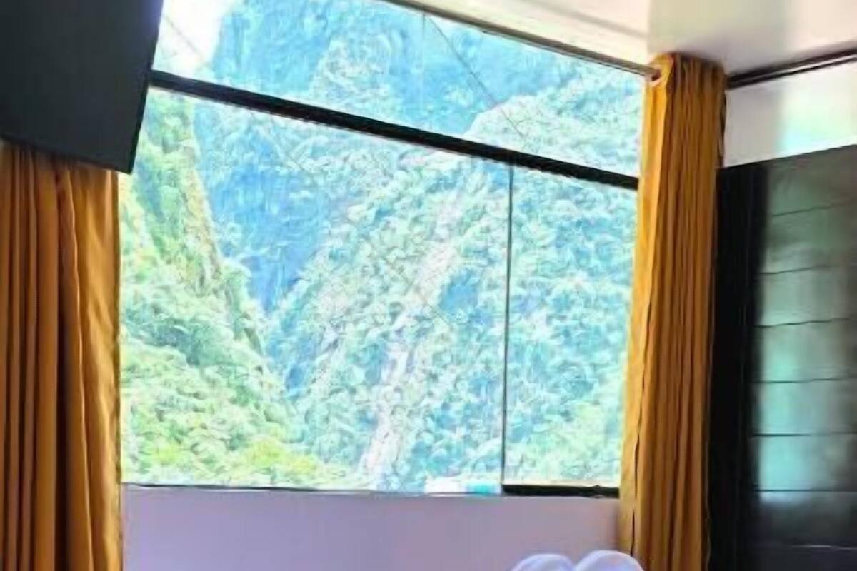Habitación de hotel con una cama grande, vista a un paisaje montañoso y cortinas en la ventana.