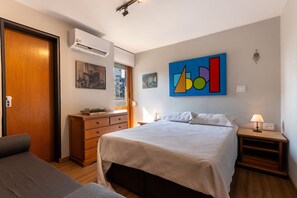 Quarto com cama, cômoda, mesa de cabeceira e ar-condicionado fixado na parede.