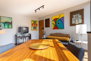 Uma sala de estar moderna com uma mesa de jantar de madeira, uma televisão e diversas obras de arte nas paredes.