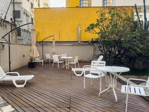 An outdoor patio with white plastic furniture, a yellow wall, and a cactus plant. - Apto em Campo Belo 20min Aeroporto CGH (São Paulo)