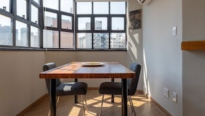A room with a wooden table, black chairs, a city view through large windows, and an air conditioning unit on the wall. - Apto em Campo Belo 20min Aeroporto CGH (São Paulo)