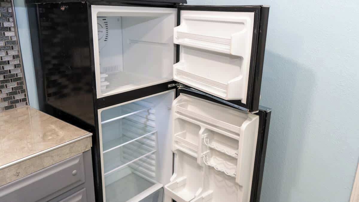 A black refrigerator with multiple shelves and drawers, located in a kitchen with a tiled backsplash and a marble countertop.