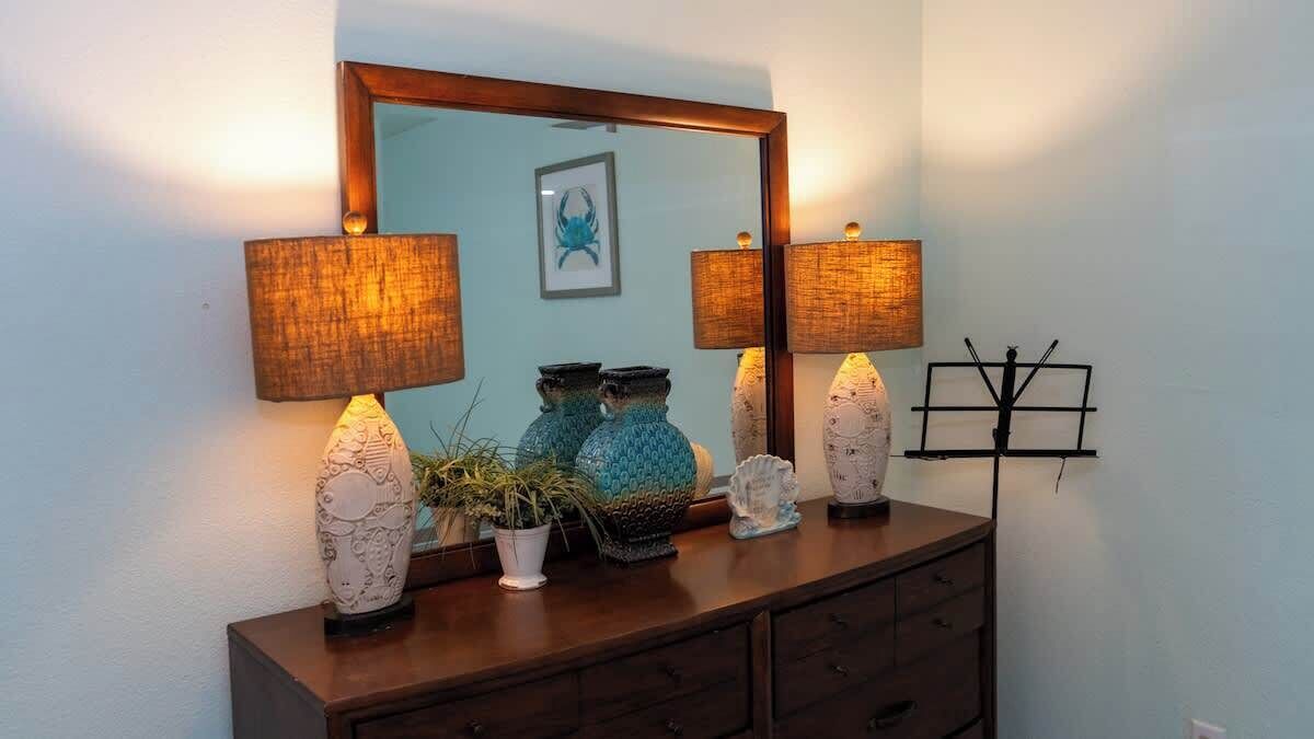 A wooden dresser with two lamps, decorative vases, and a framed mirror.