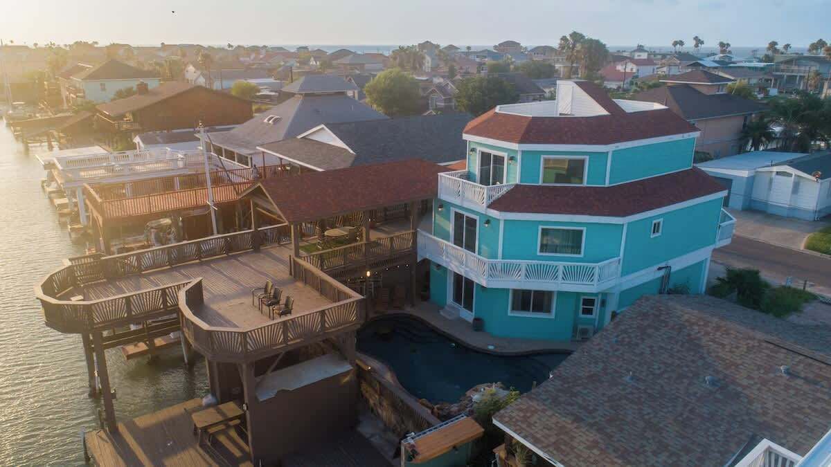 A multi-story house with a pool, a dock, and a balcony.