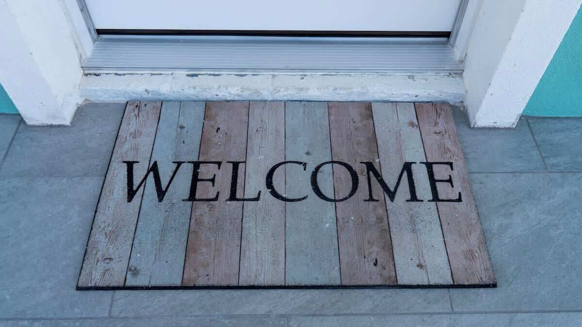 A wooden welcome mat with the word "WELCOME" in front of a door.