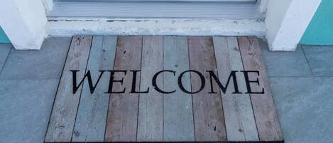 Un tappetino di legno con la scritta "WELCOME" davanti a una porta.