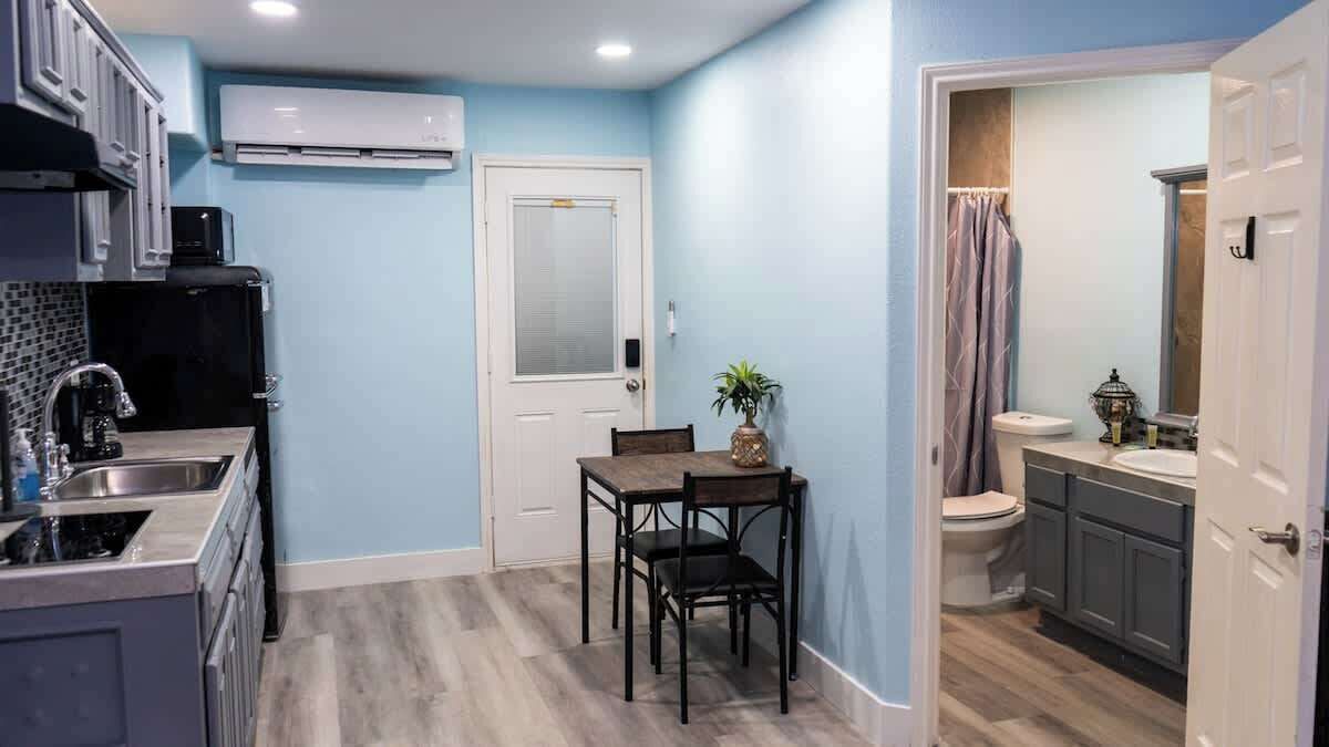 A compact kitchen with a dining area, a white door, and a bathroom with a shower curtain.